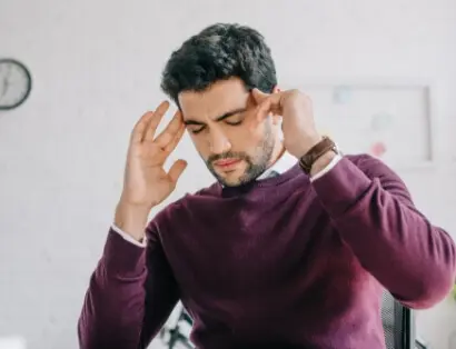 Man holding temples in pain, experiencing headache or migraine, representing pain relief services at Messina Acupuncture in Setauket, NY